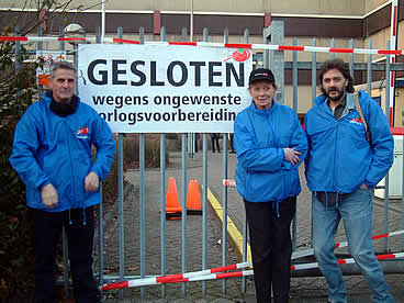 Aktievoerders bij de hekken met bord "gesloten wegens ongewenste oorlogsvoorbereidingen"